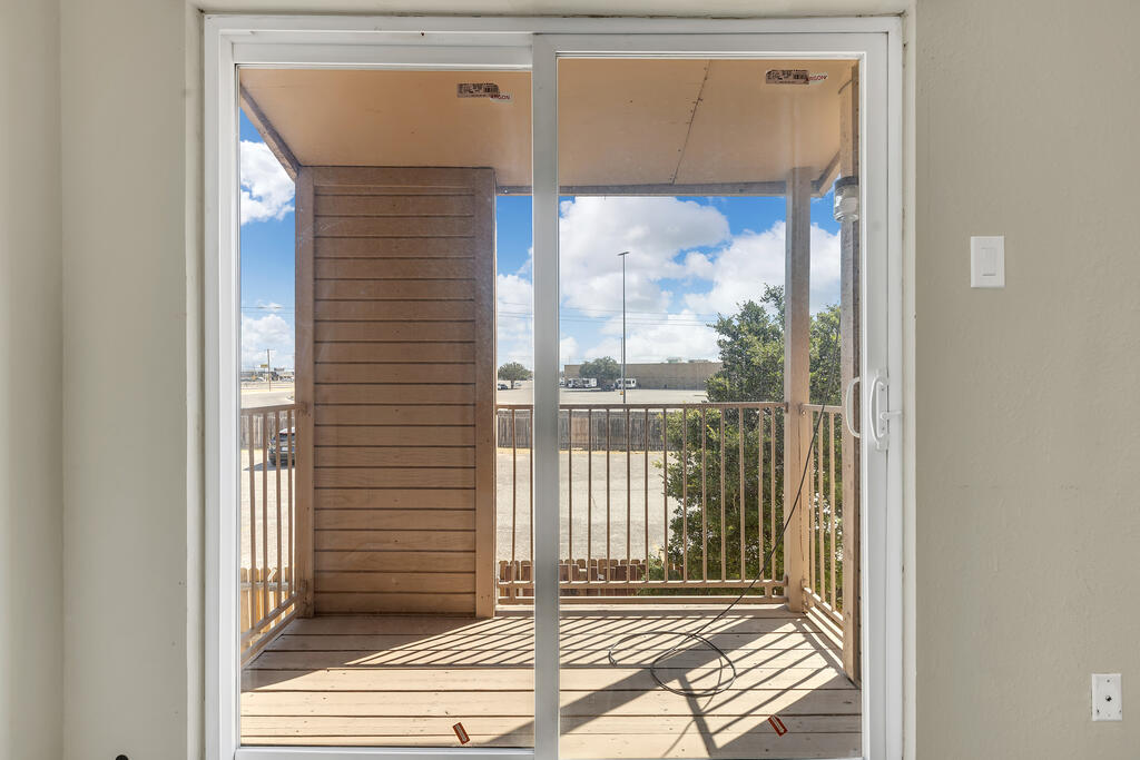 Sliding glass doors overlook a covered balcony with wooden railings and a loose cable on the floor.