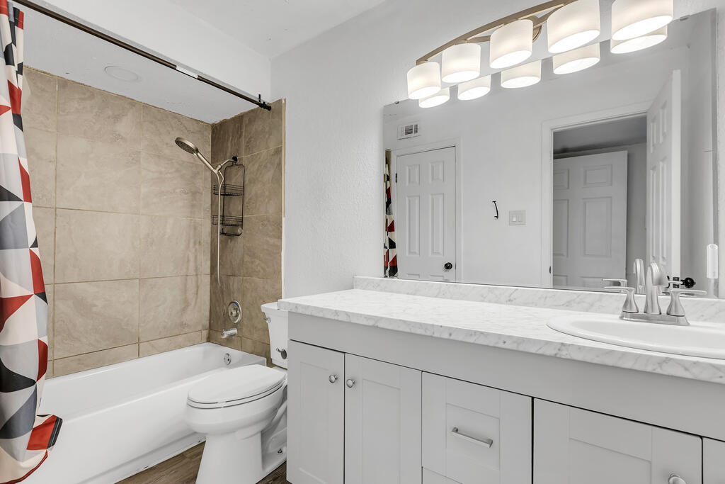 Bathroom with beige tiled tub surround and a long white vanity beneath a large mirror.