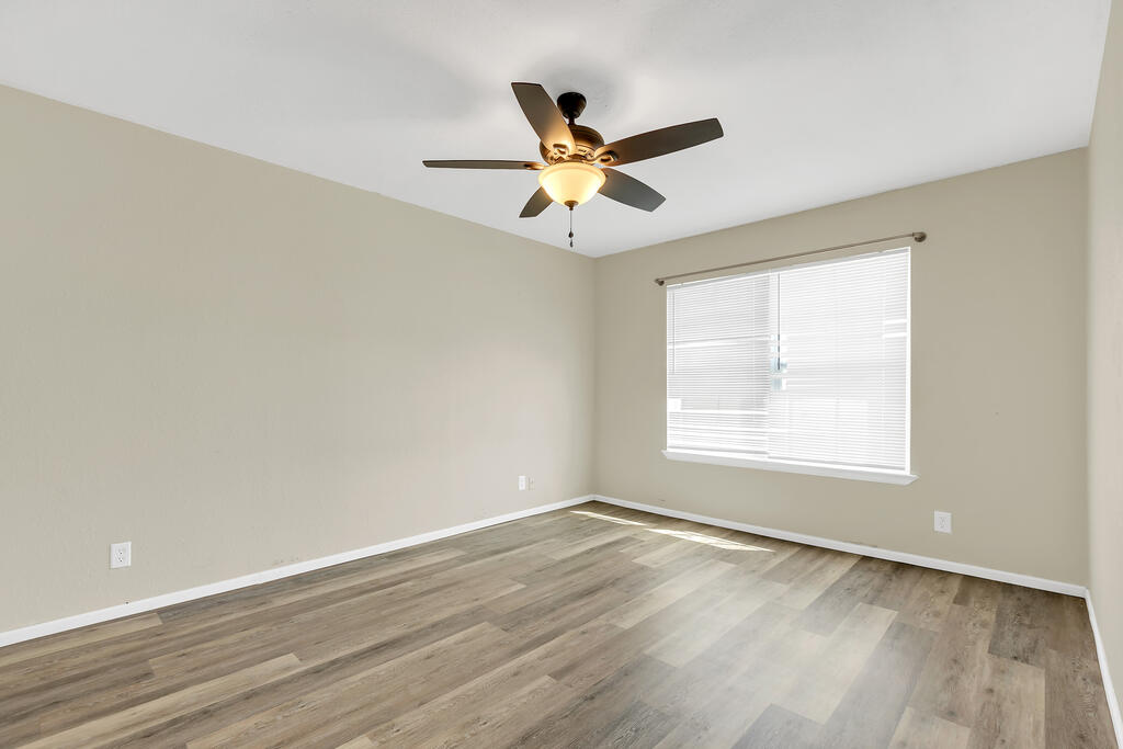 Empty room with plank flooring, a ceiling fan, and a window with blinds.