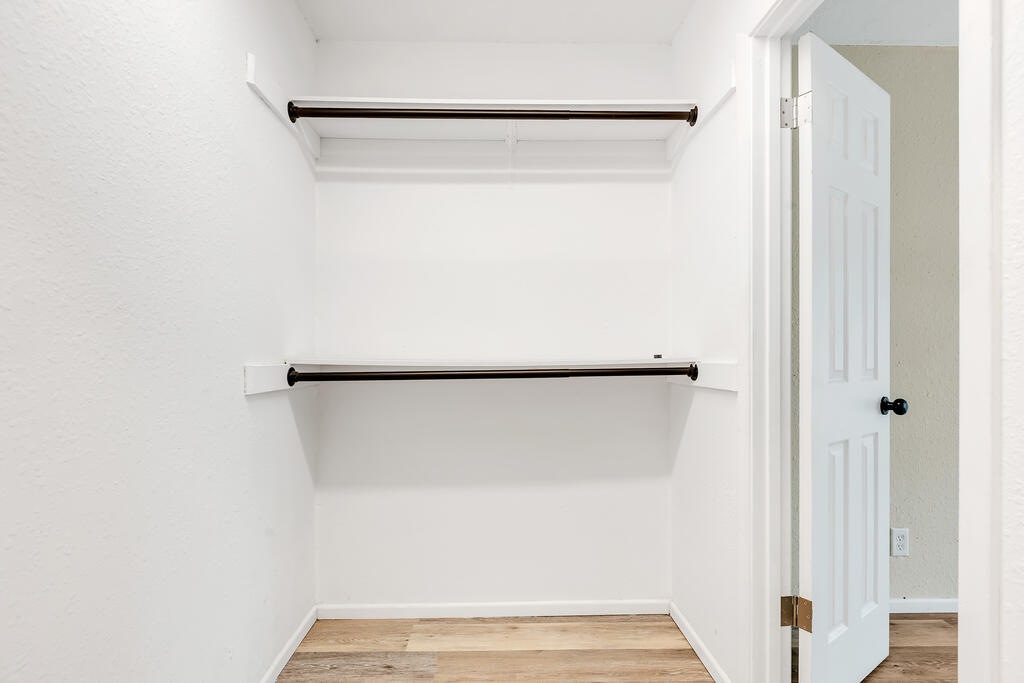 Empty white walk-in closet with two hanging rods, a high shelf, and wood-look flooring.