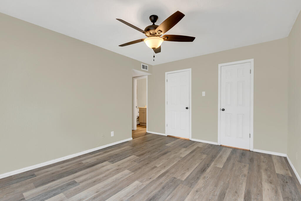 Empty room with gray plank flooring, a lit ceiling fan, and two white doors.