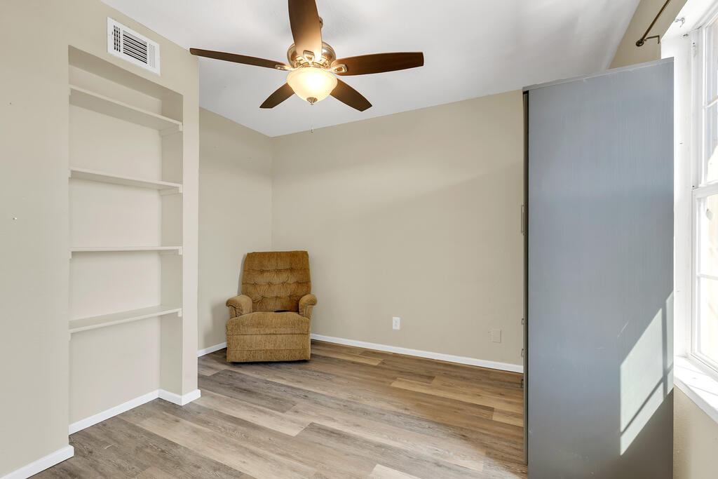 Interior room with built-in shelving, a ceiling fan, plank flooring, and an upholstered chair.