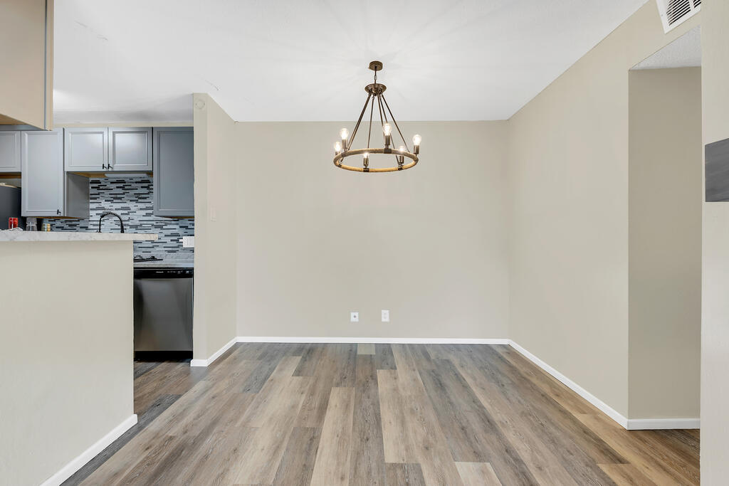 Empty dining area with a bronze ring chandelier and gray wood-look flooring beside the kitchen.