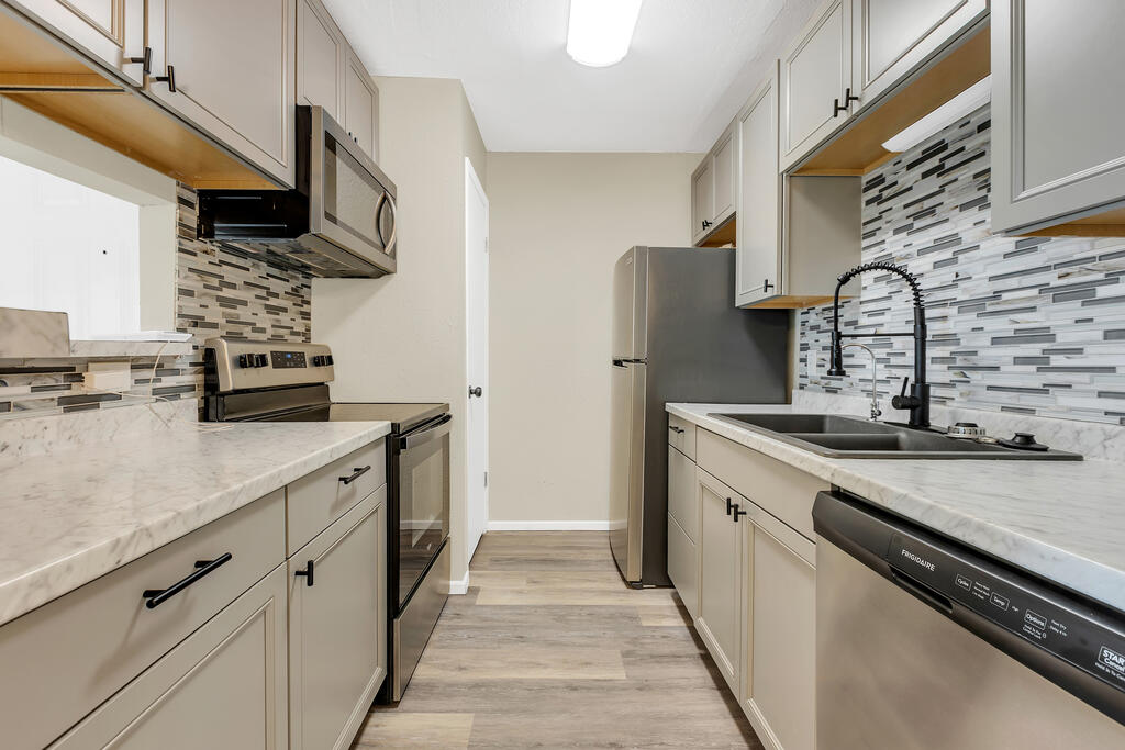Galley kitchen with light cabinets, stone counters, mosaic backsplash, and stainless steel appliances.