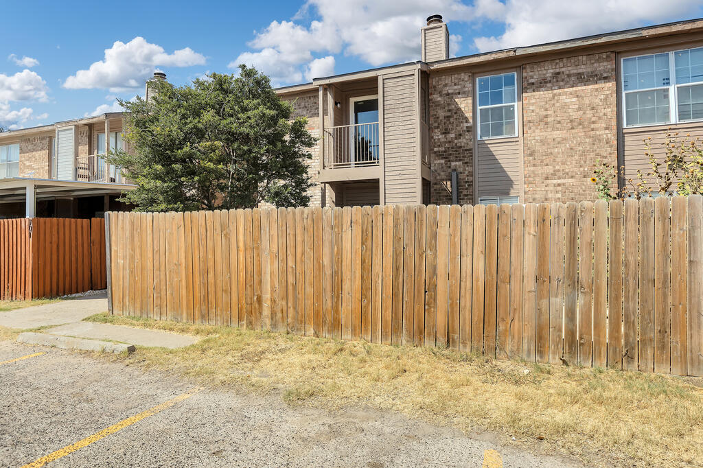 Two-story brick apartment building behind a tall wooden privacy fence.