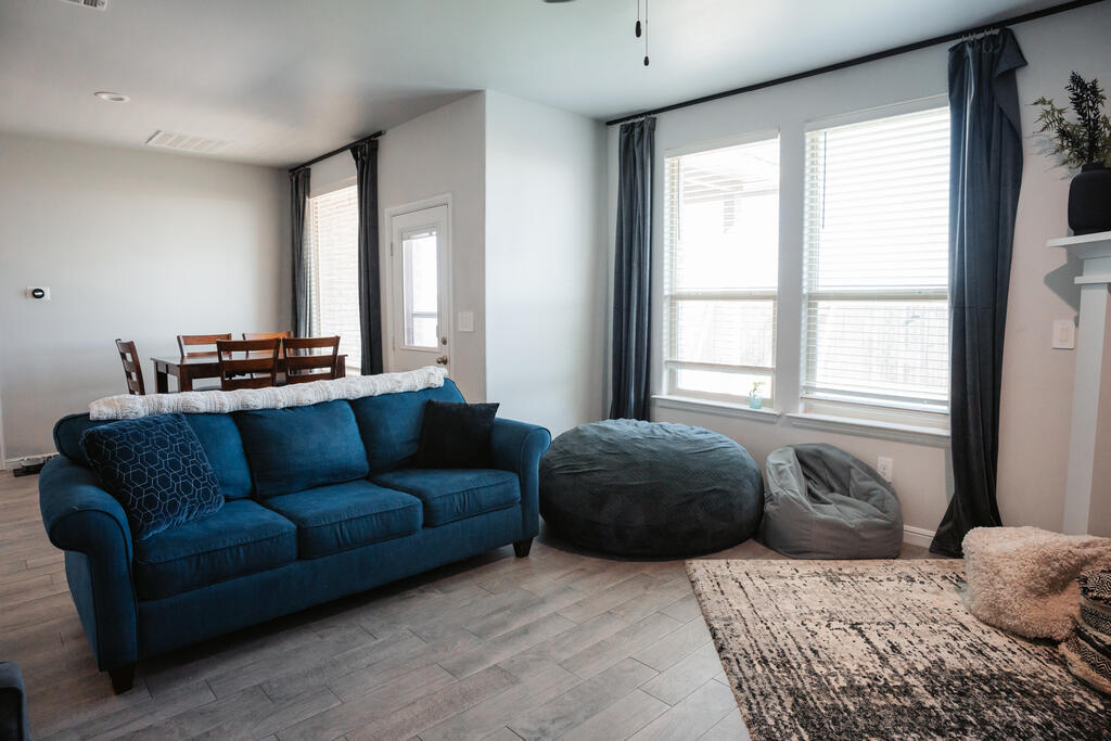 Living room with a blue sofa, dark ottomans, large windows, and an adjacent dining area.