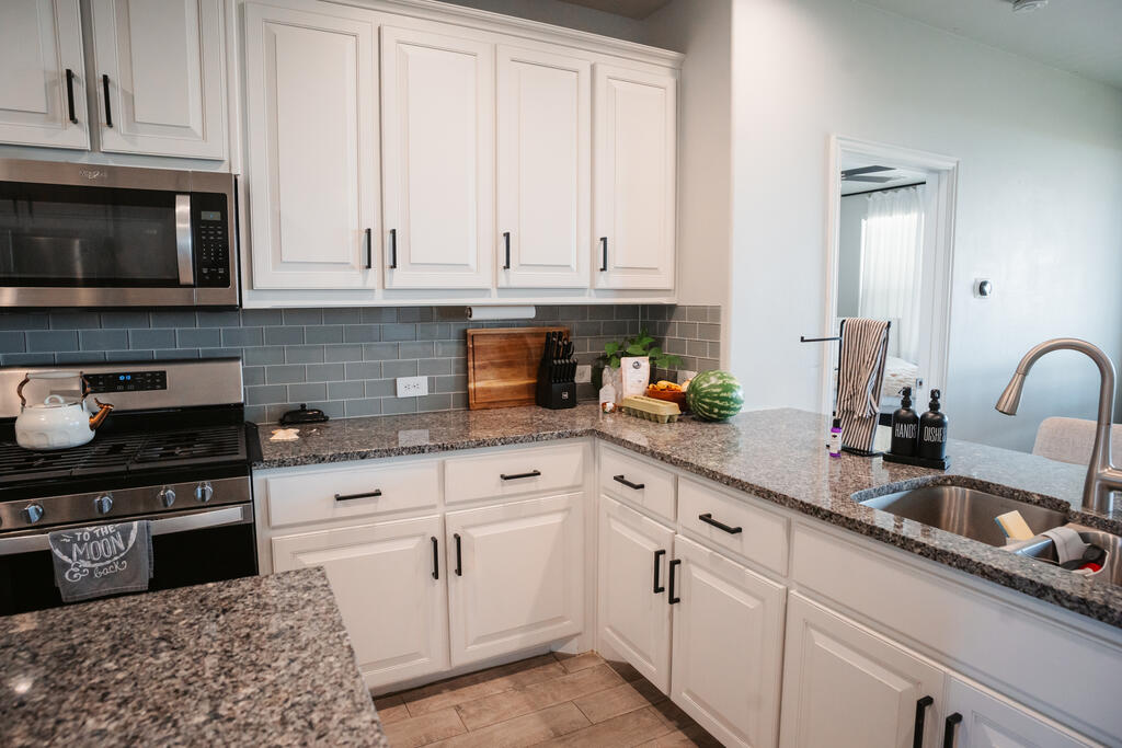 Kitchen with white cabinetry, granite counters, gray tile backsplash, and stainless steel appliances.