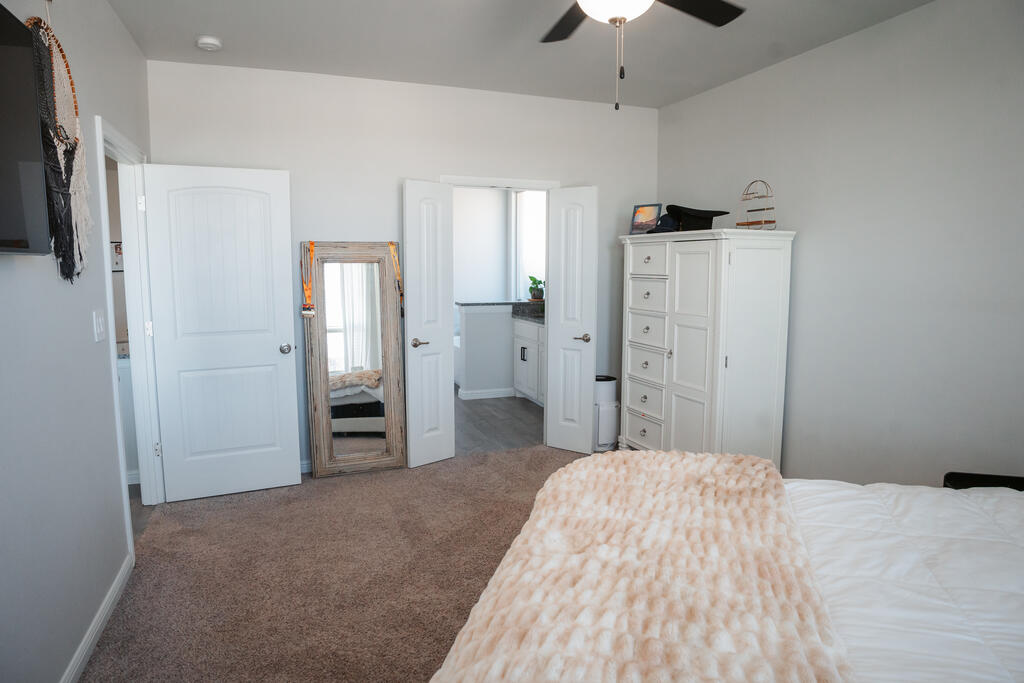 Bedroom with beige carpet, white bed and dresser, and open doors to an adjoining bathroom.