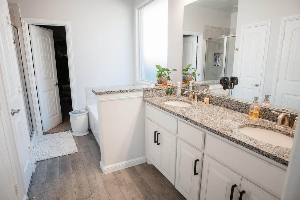 Bathroom with a double-sink granite vanity, large mirror, and gray tile flooring.