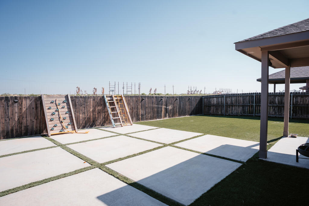 Fenced backyard with a covered patio, concrete pavers, artificial turf, and a climbing wall.