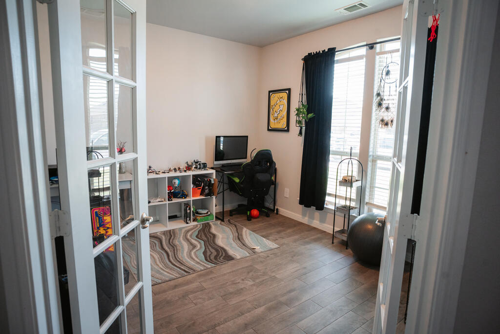 Home office with a gaming chair, desk, cubby shelves, patterned rug, and tall windows.