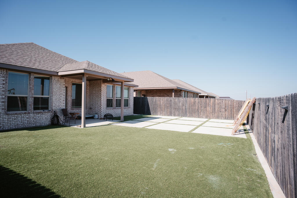 Fenced backyard with artificial turf, a covered brick patio, and a wooden play structure.