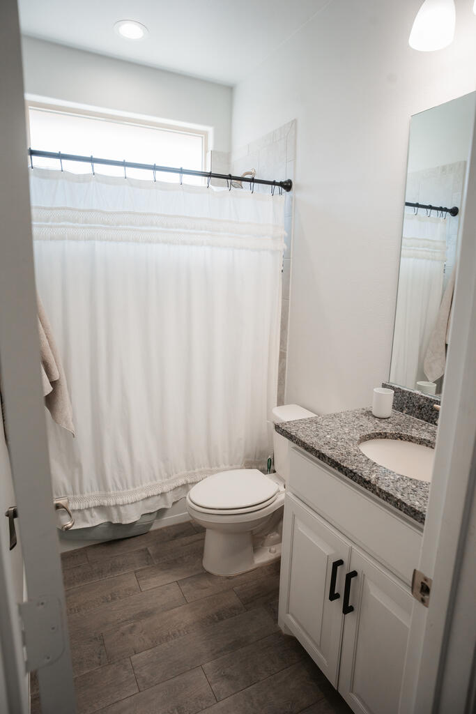 Bathroom with a curtained tub and shower, granite-topped vanity, and gray-brown tile floor.