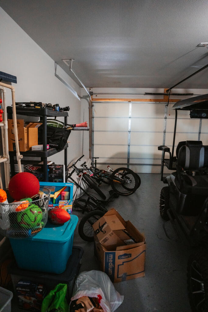 Cluttered garage with bicycles, toys, storage bins, and a riding mower.