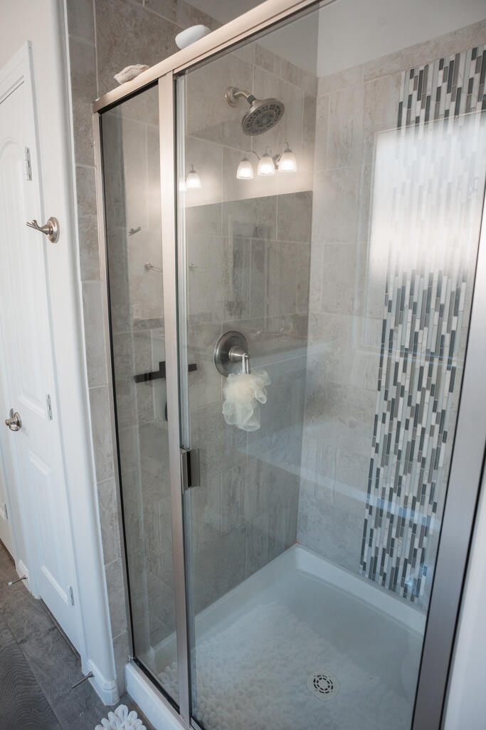 Tiled shower with glass doors, a large showerhead, and a vertical mosaic accent strip.