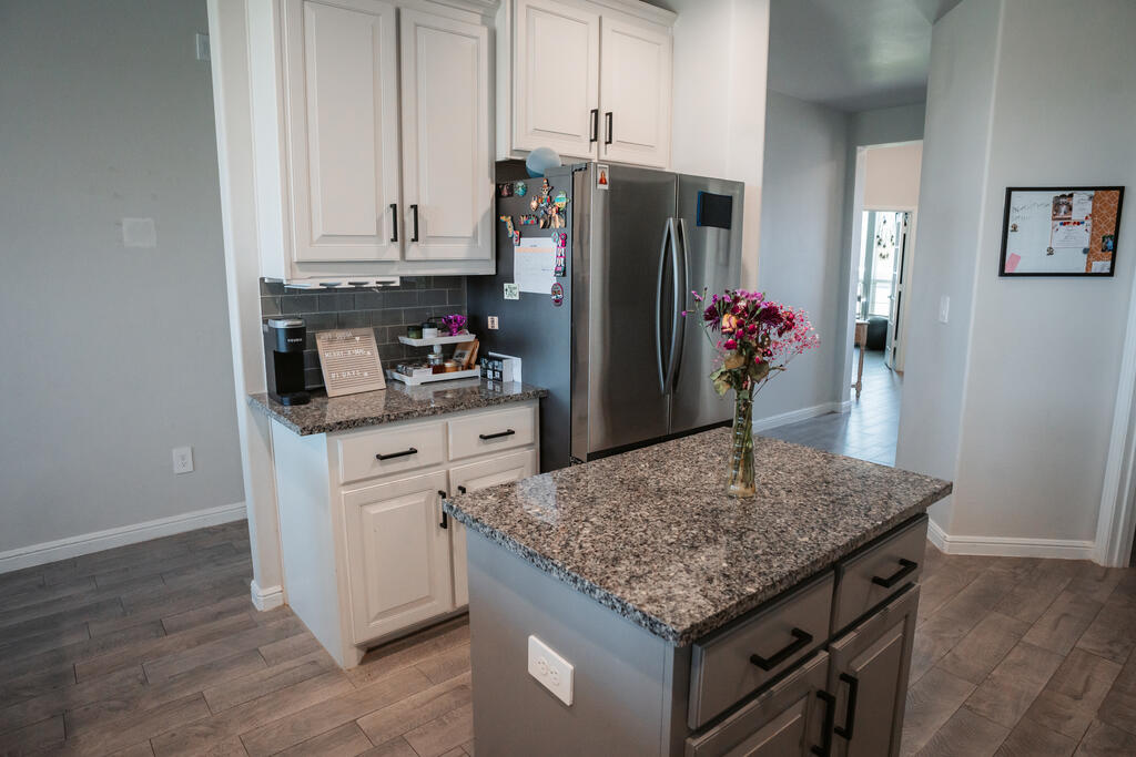 Kitchen with a granite island, white cabinets, stainless steel refrigerator, and flowers.