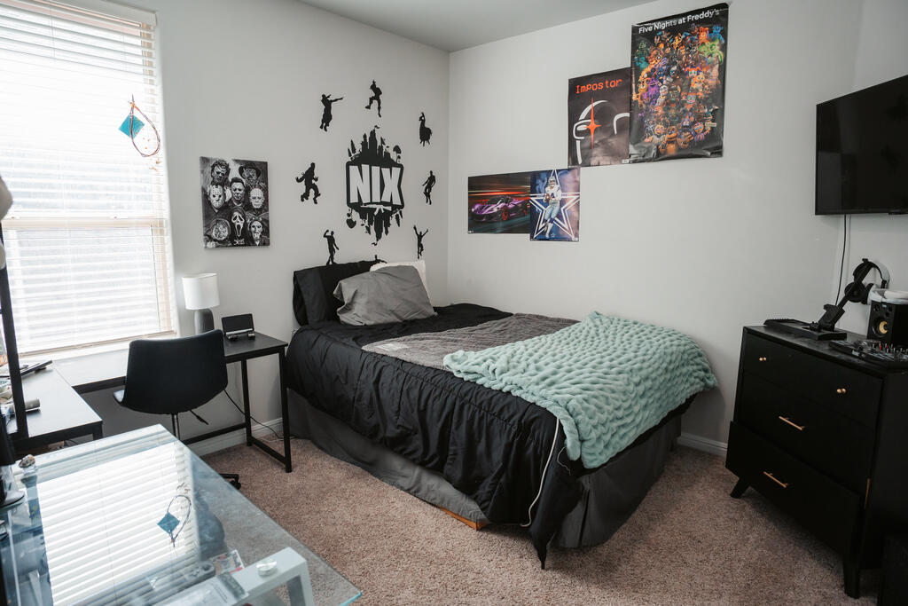 Bedroom with dark bedding, a mint-green throw, gaming posters, and a desk beside a bright window.