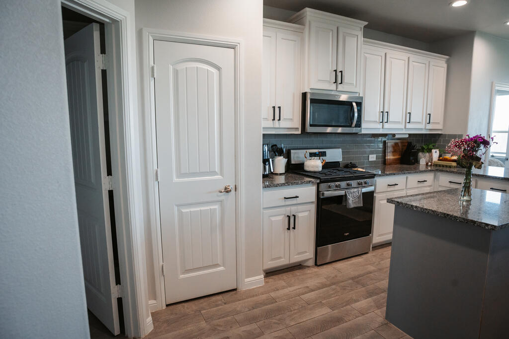 Kitchen with white cabinetry, stainless steel appliances, and a granite island topped with flowers.