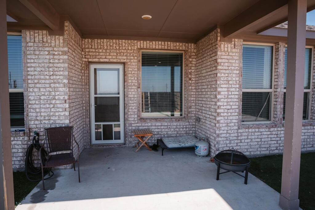 Covered brick patio with a screened door, seating, pet bed, and round fire pit.