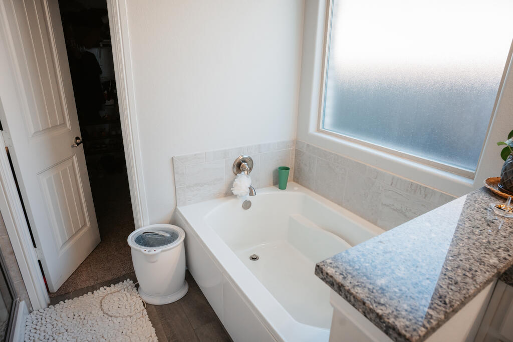 Bathroom soaking tub beneath a frosted window, with light tile and a granite countertop.
