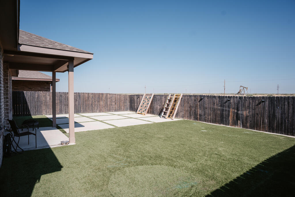 Fenced backyard with green turf, a covered patio, and a concrete patio area.