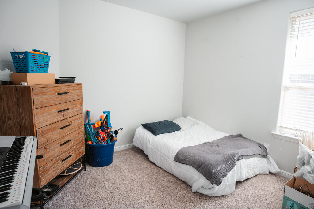 Bedroom with a single bed, wooden dresser, and children's toys in a blue bin.