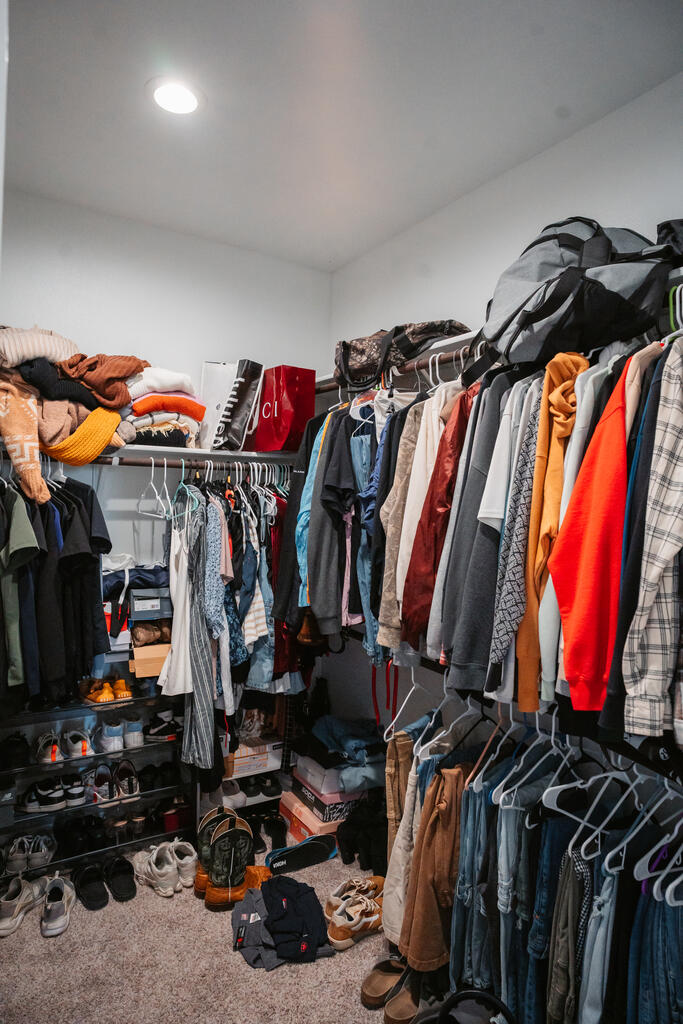 Walk-in closet packed with hanging clothes, shelves of folded items, and shoes covering the floor.
