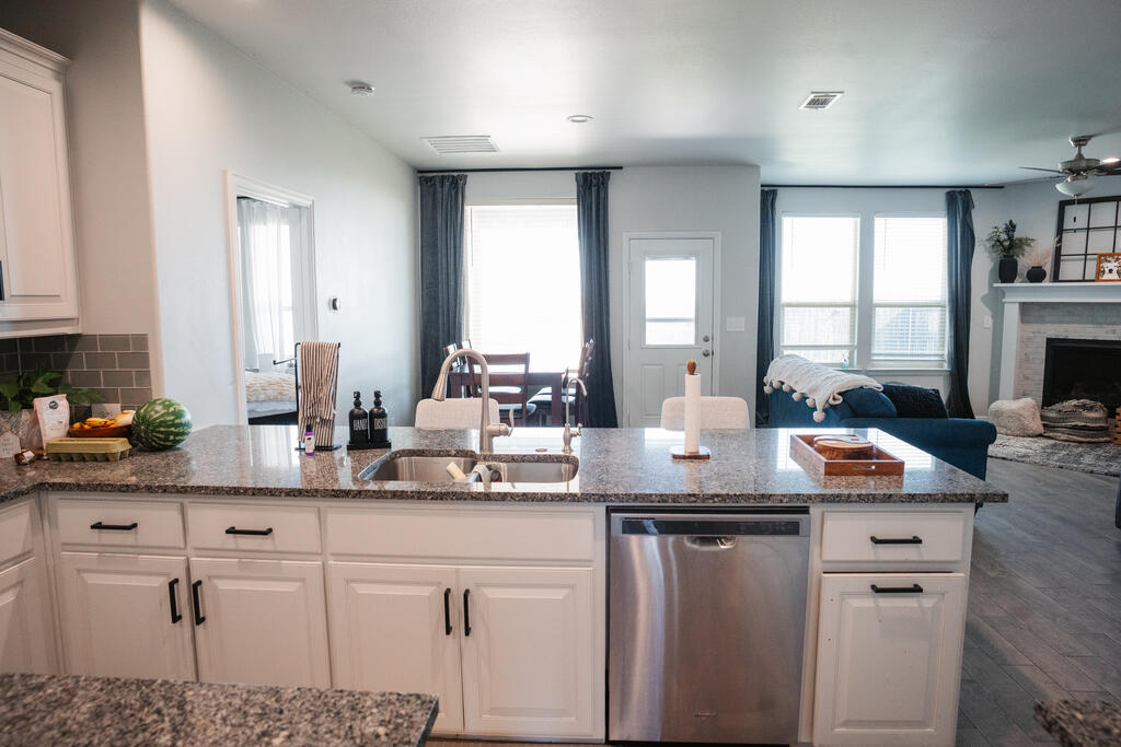 Open-plan kitchen with a granite island, white cabinets, and stainless-steel dishwasher.