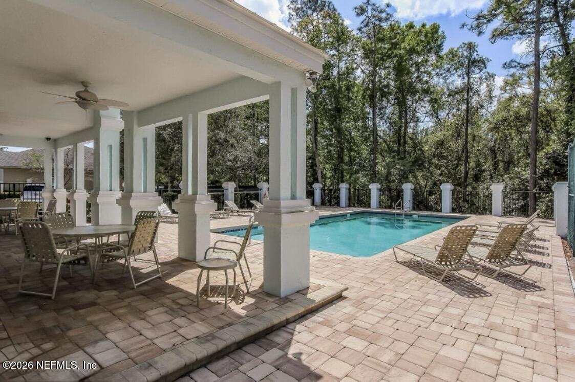 Outdoor pool beside a covered patio with white columns and lounge chairs on the paved deck.