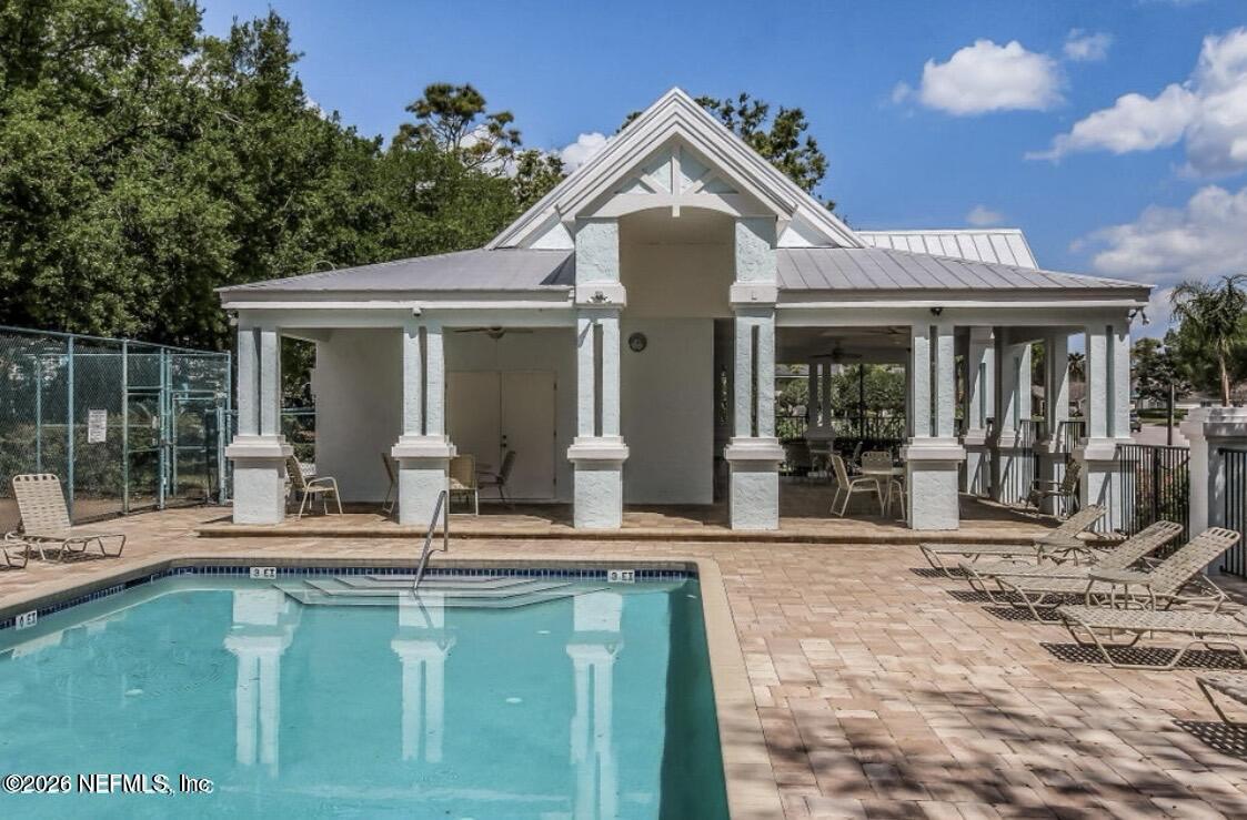Swimming pool and paved deck beside a white covered pavilion with outdoor seating.