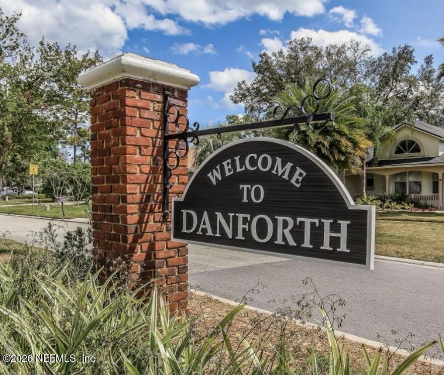 Danforth entrance sign beside a red brick pillar, with a house and trees in the background.