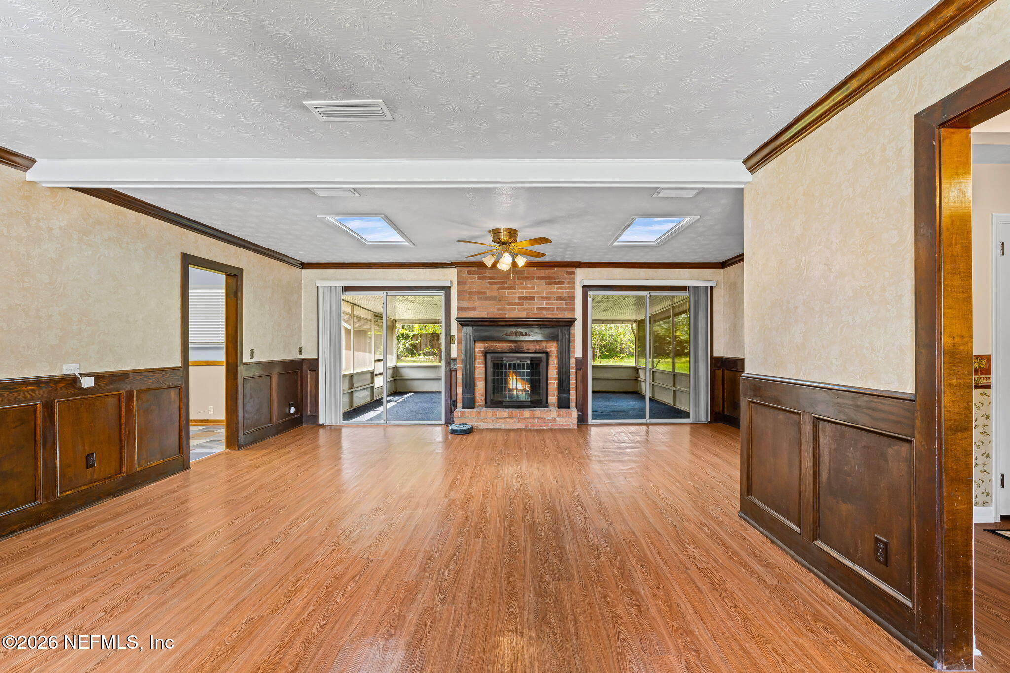 Vacant living room with a brick fireplace, wood floors, and sliding doors to enclosed sunrooms.