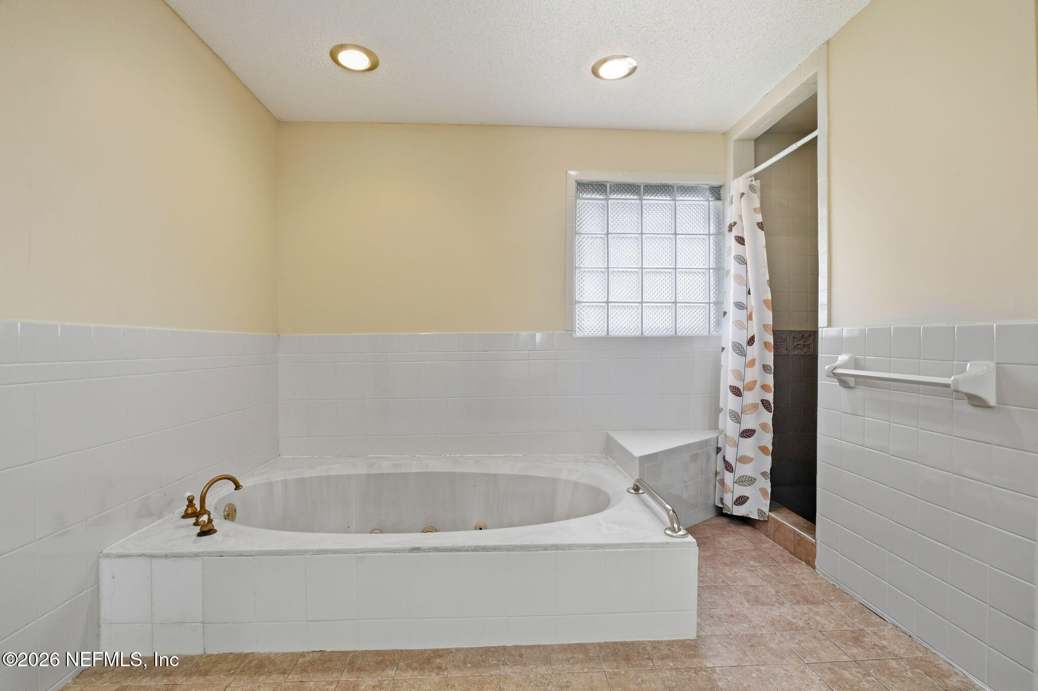 Bathroom with a built-in soaking tub, glass-block window, and tiled shower.