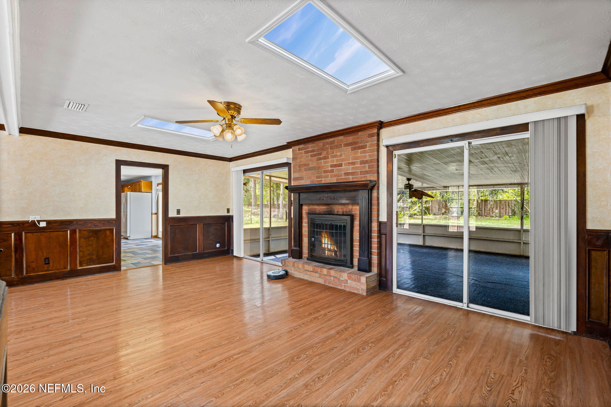 Unfurnished living room with brick fireplace, two skylights, and sliding doors to a screened porch.