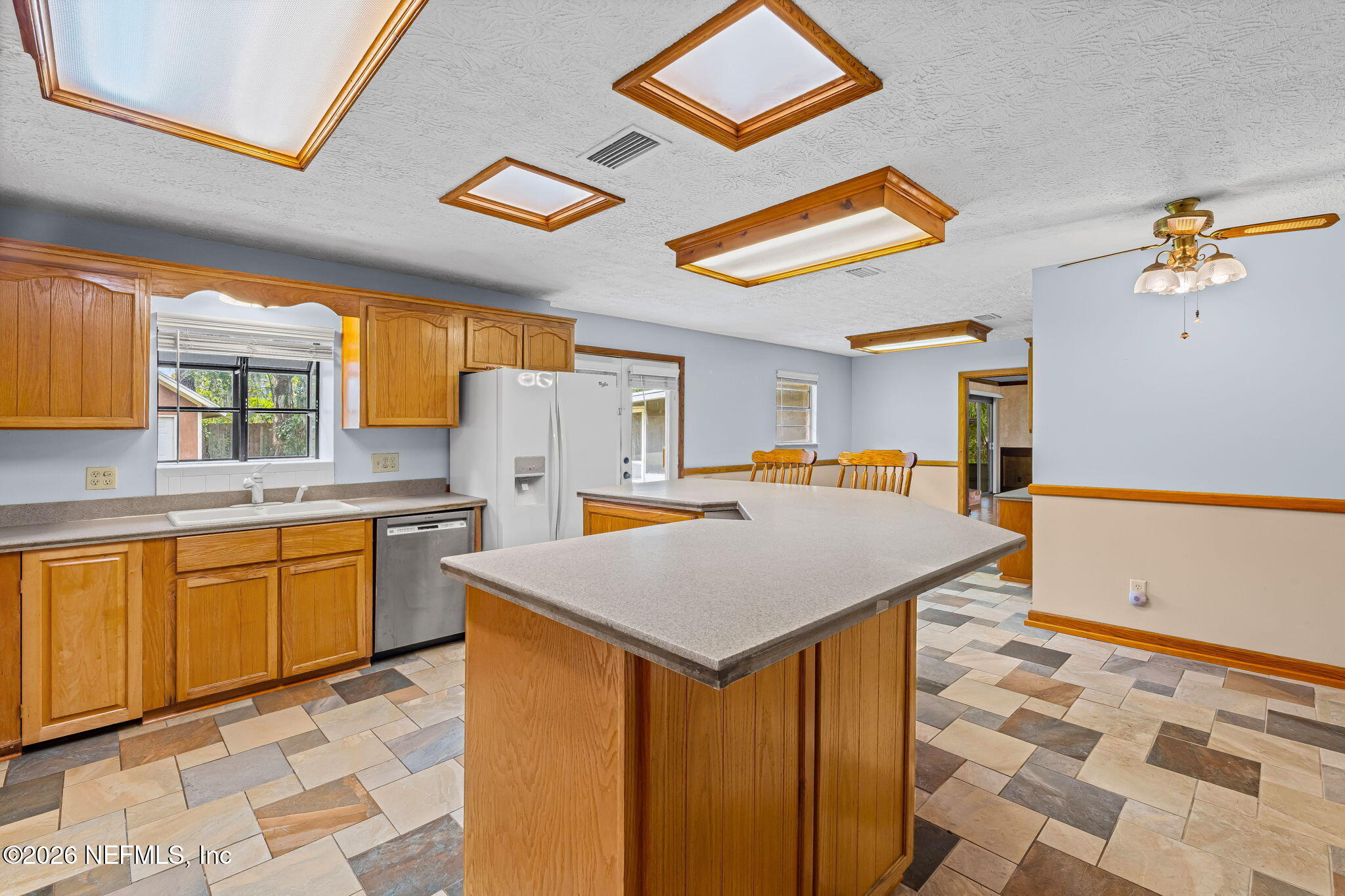Kitchen with a large gray-countertop island, honey-toned cabinets, and multicolored tile flooring.