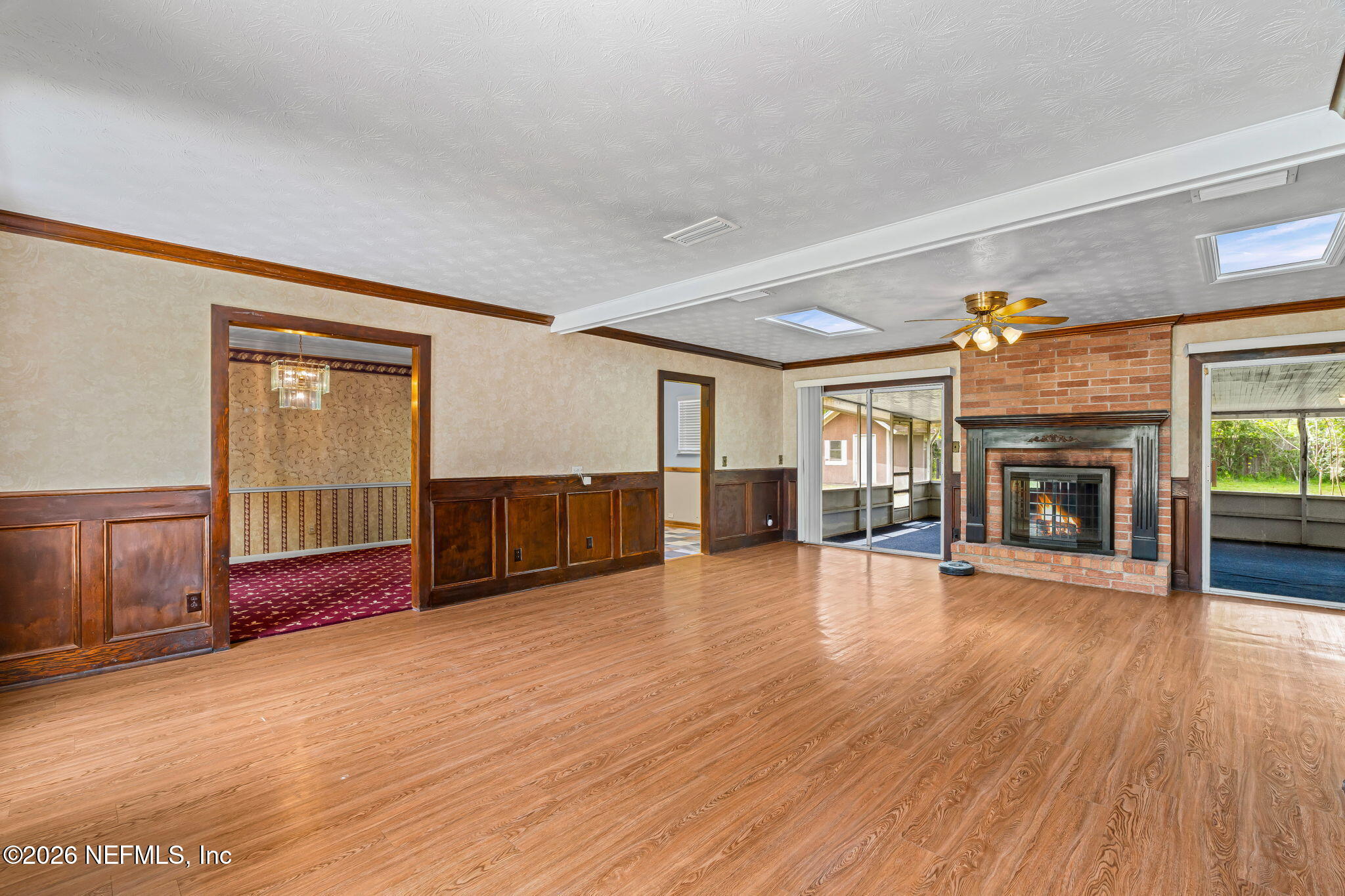 Living room with a brick fireplace, wood-look flooring, and sliding doors to a screened porch.