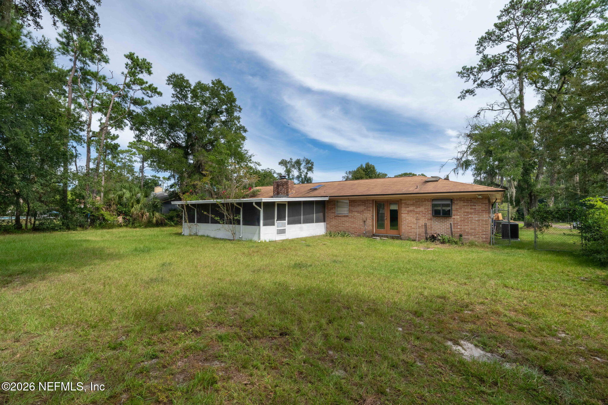 Brick home’s rear exterior with a screened porch, spacious grassy yard, and mature trees.