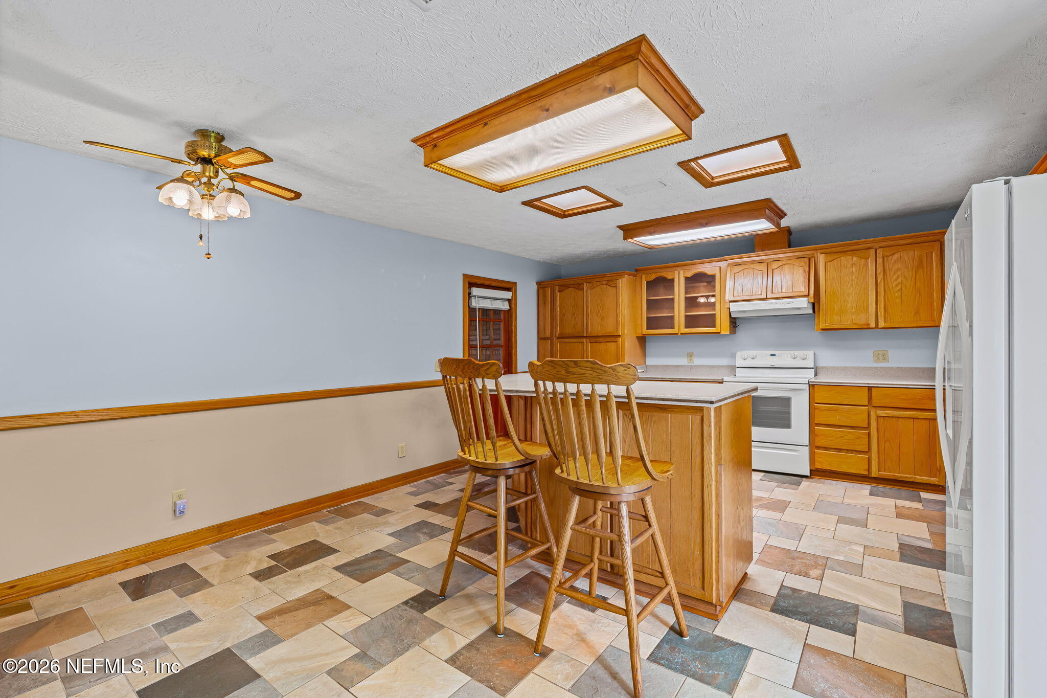 Kitchen with honey-toned wood cabinetry, a central island, wooden stools, and multicolored tile flooring.