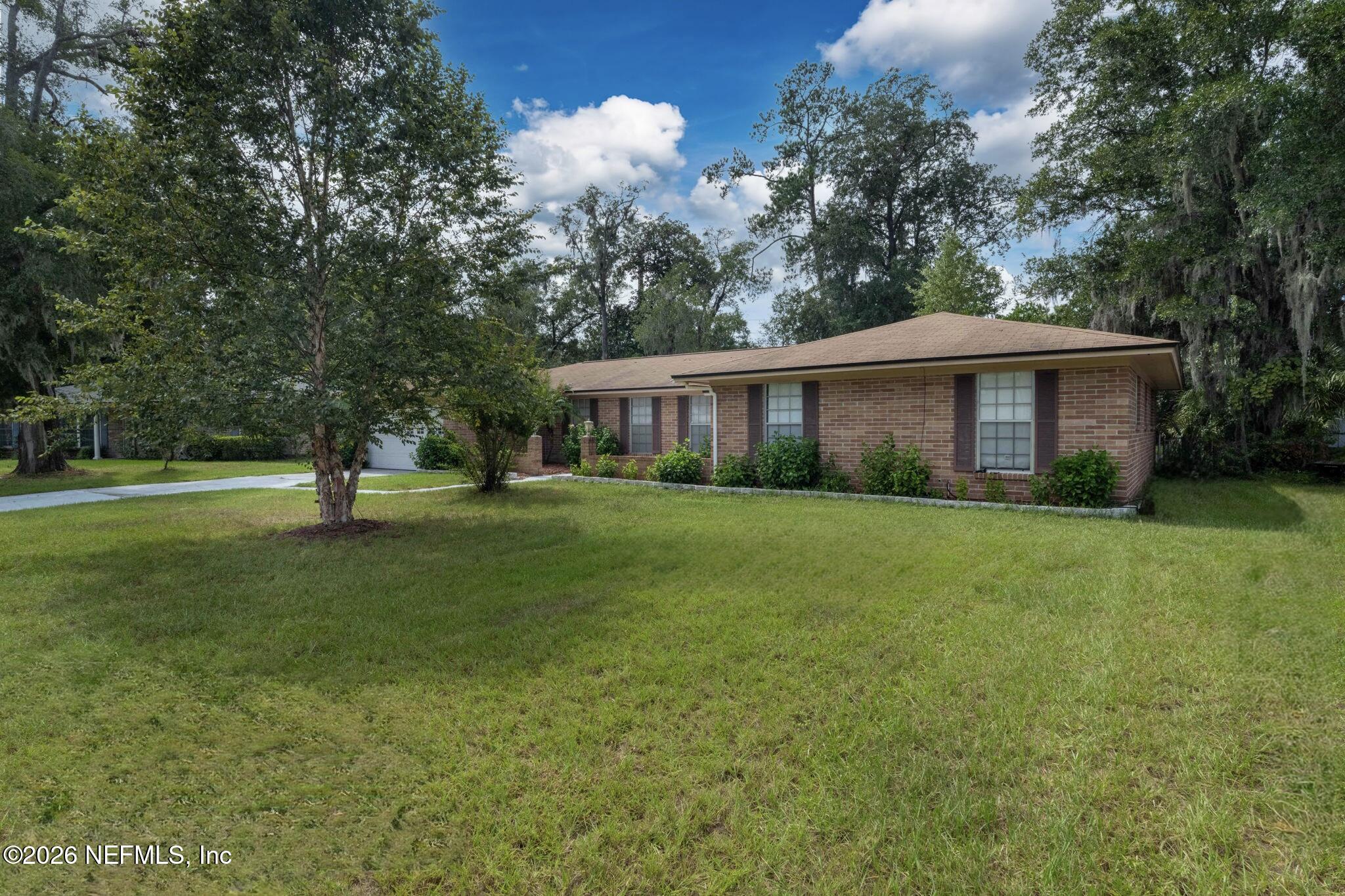 Single-story brick house with dark shutters, broad front lawn, and mature trees.