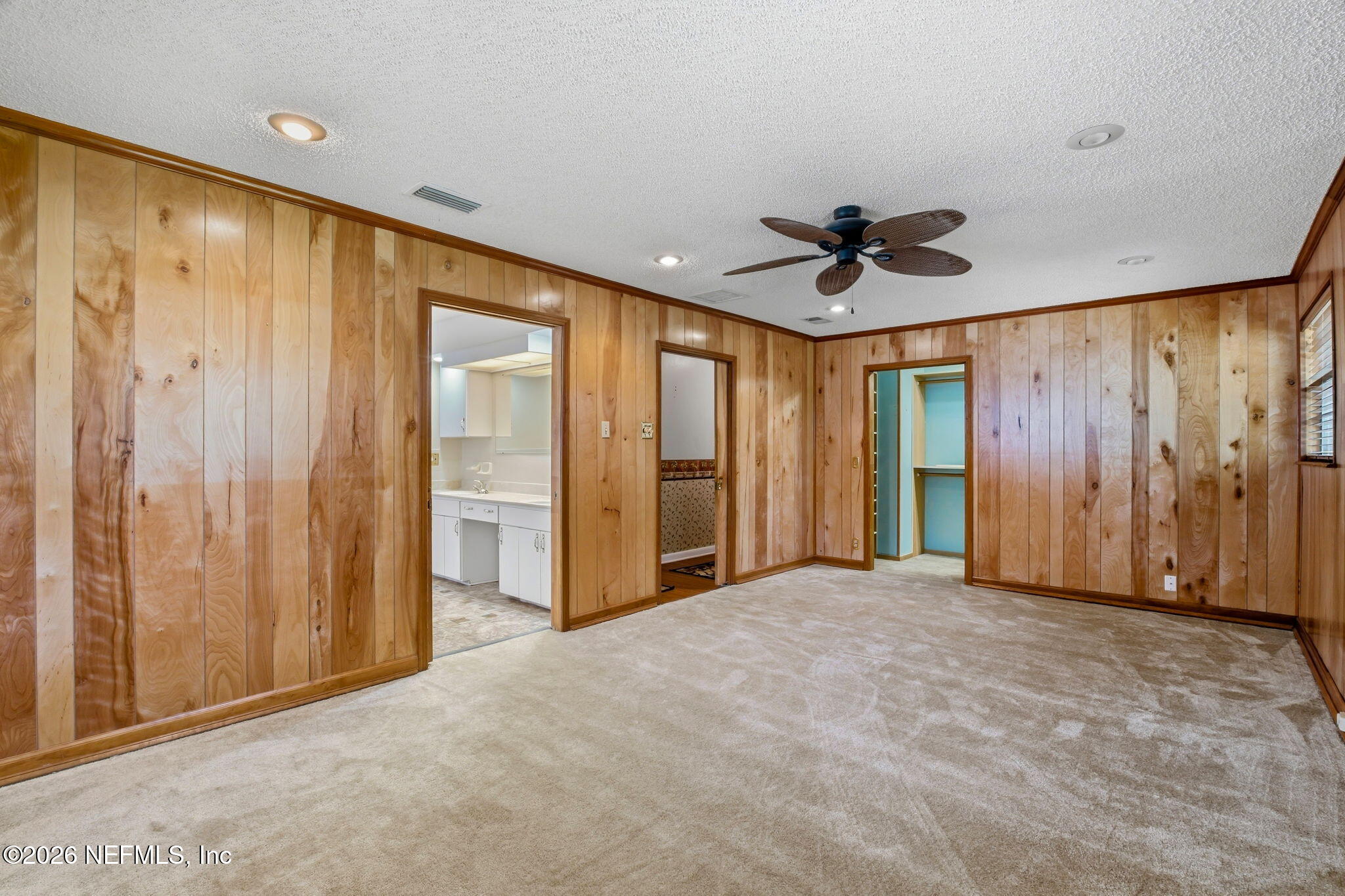 Empty bedroom with wood-paneled walls, beige carpet, and a ceiling fan.