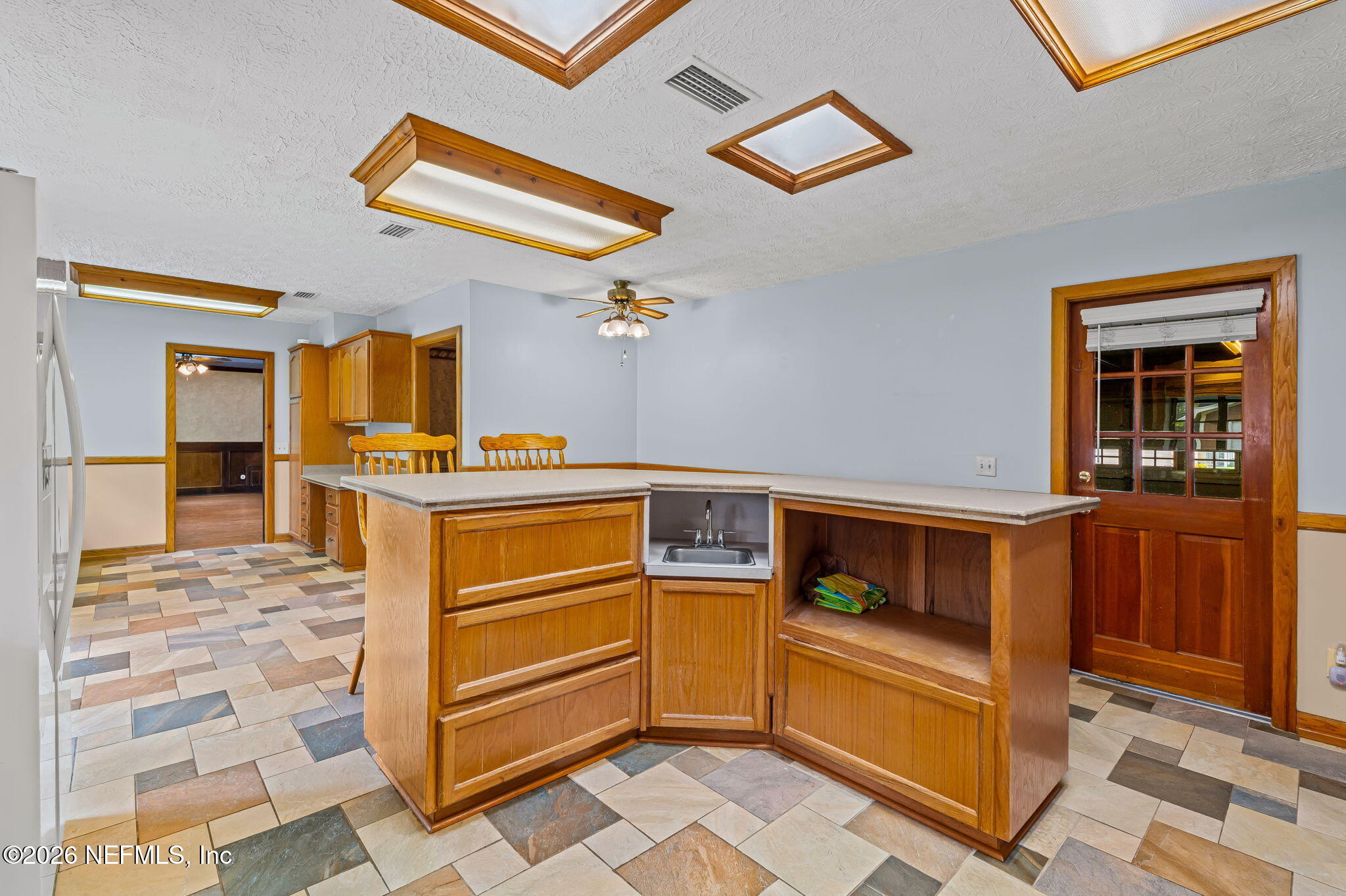 Kitchen with a large wood peninsula, built-in sink, open shelving, and multicolored tile floor.