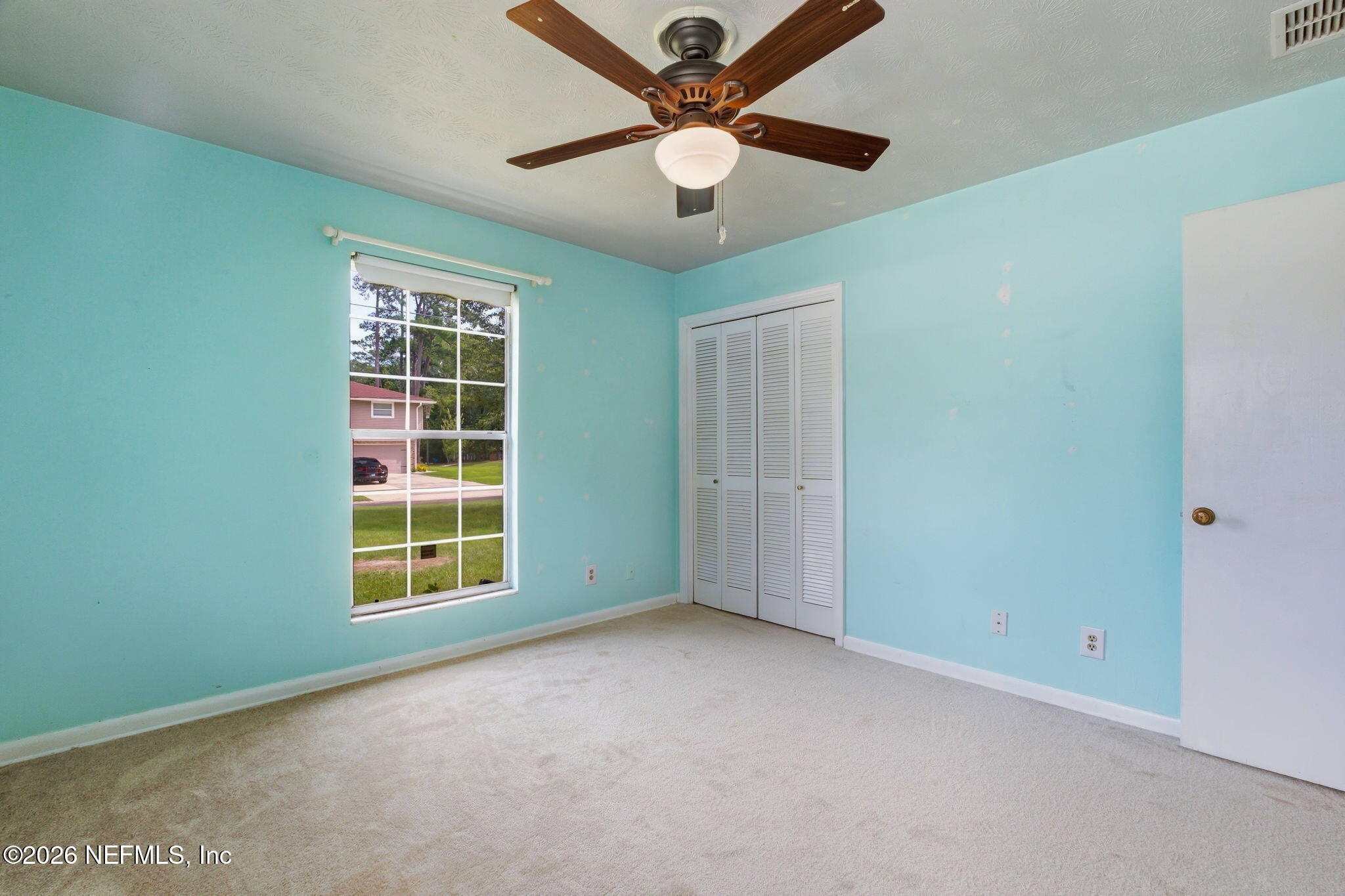 Empty bedroom with turquoise walls, beige carpet, a large window, and a dark wood ceiling fan.