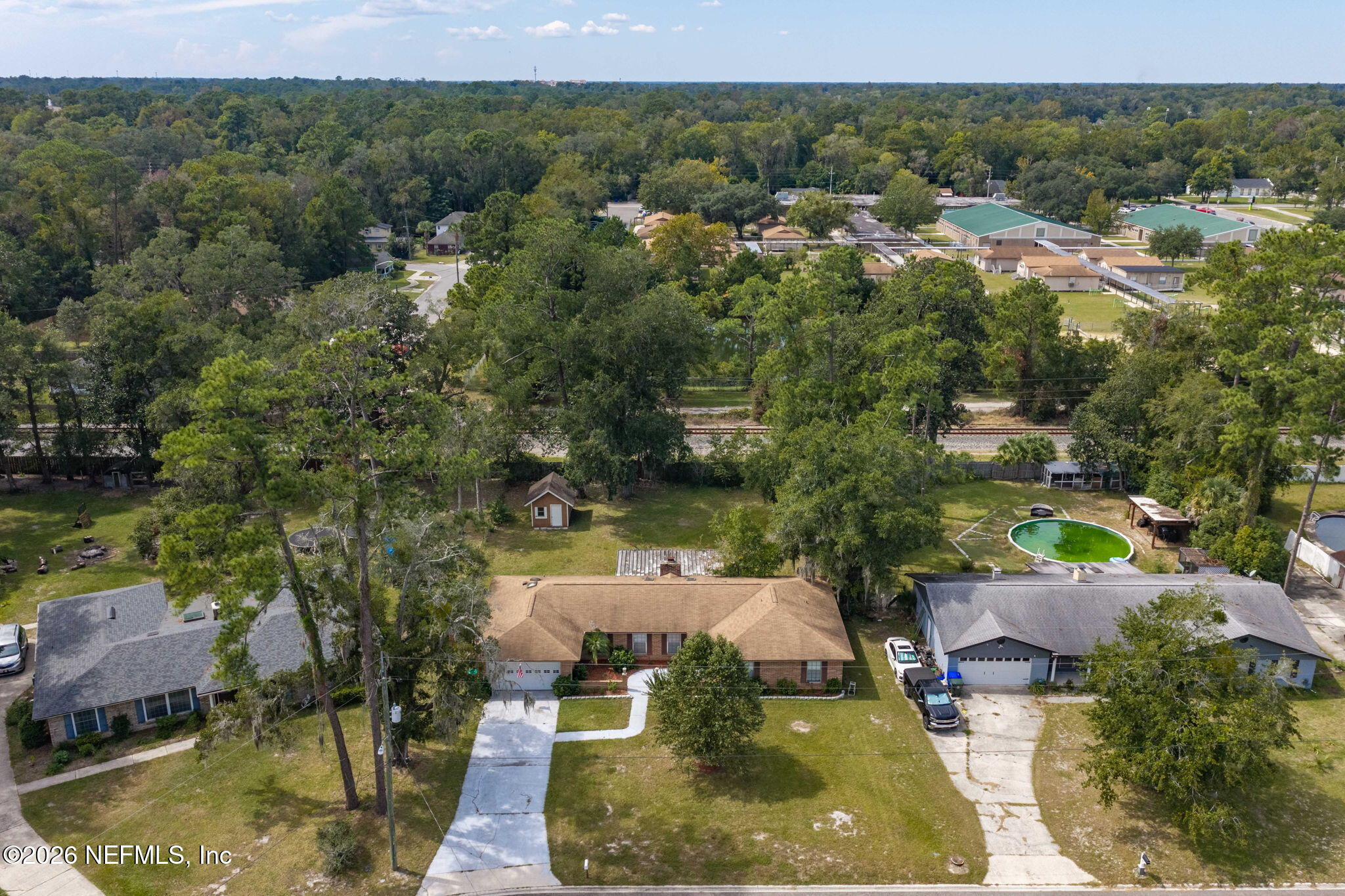 Aerial view of a single-story brick house with a tan roof, large yard, and mature trees.