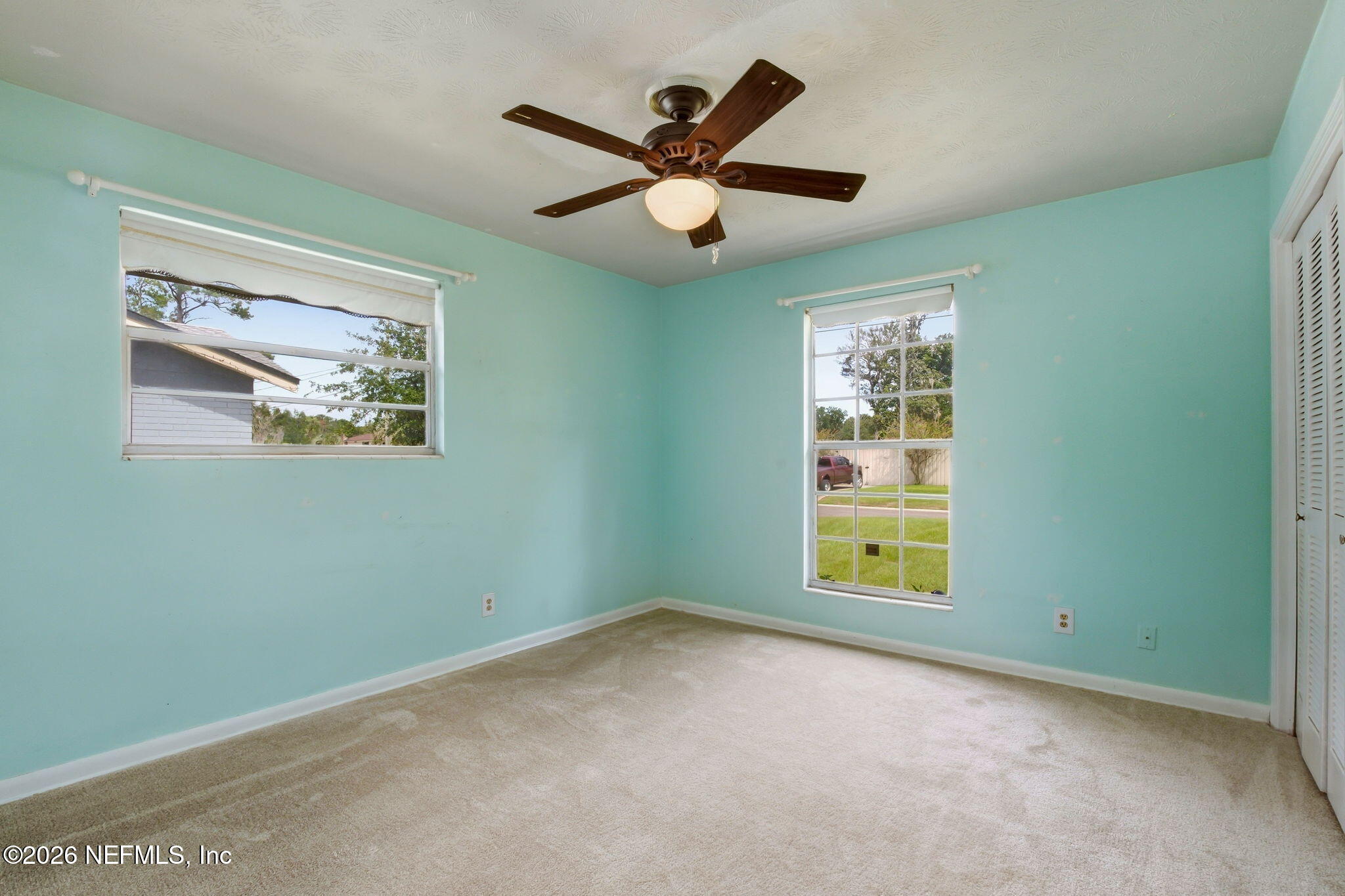 Vacant bedroom with aqua walls, beige carpet, two windows, and a dark wood ceiling fan.
