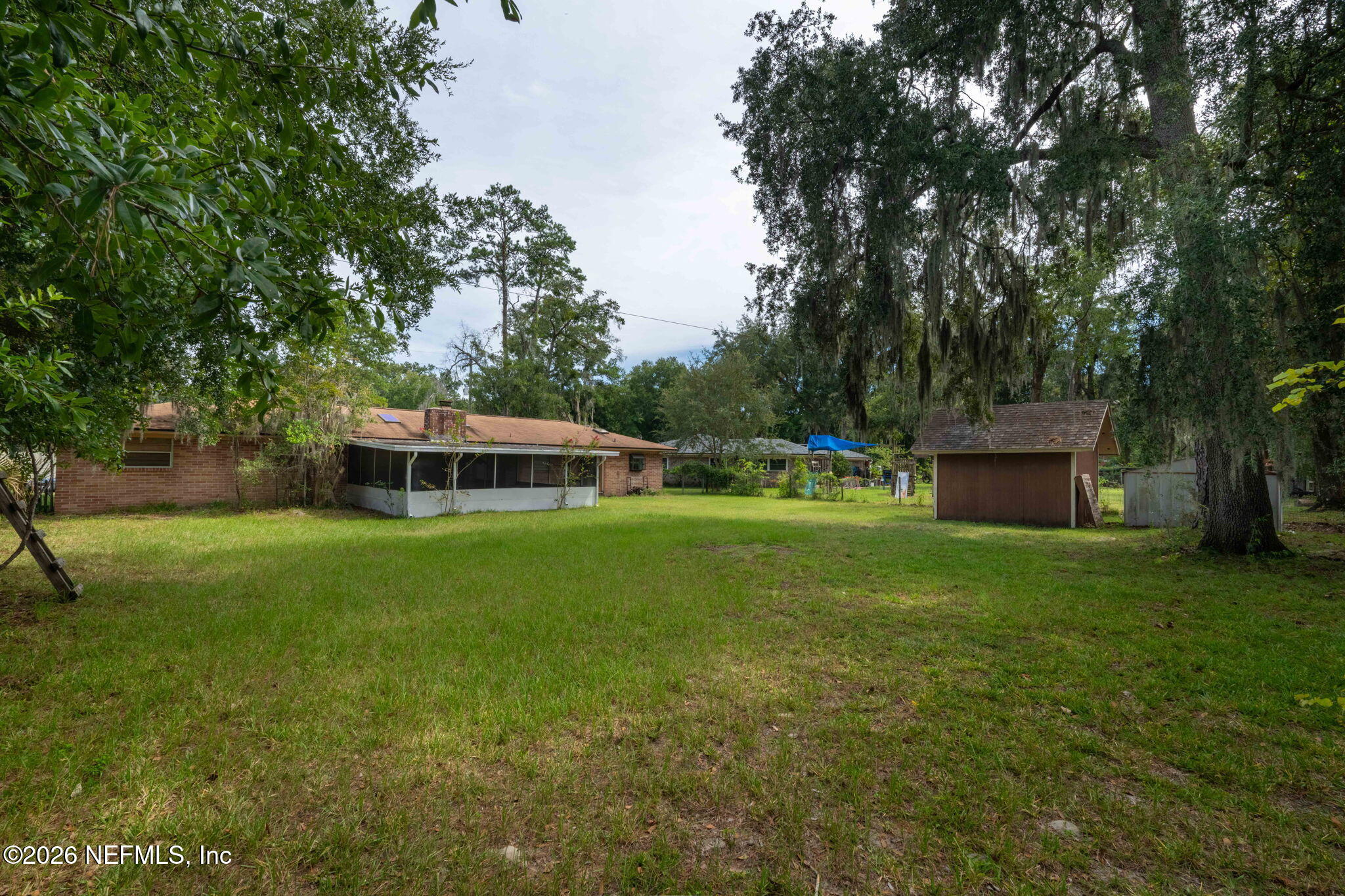 Rear yard with a brick home, screened porch, detached shed, and mature oak trees.