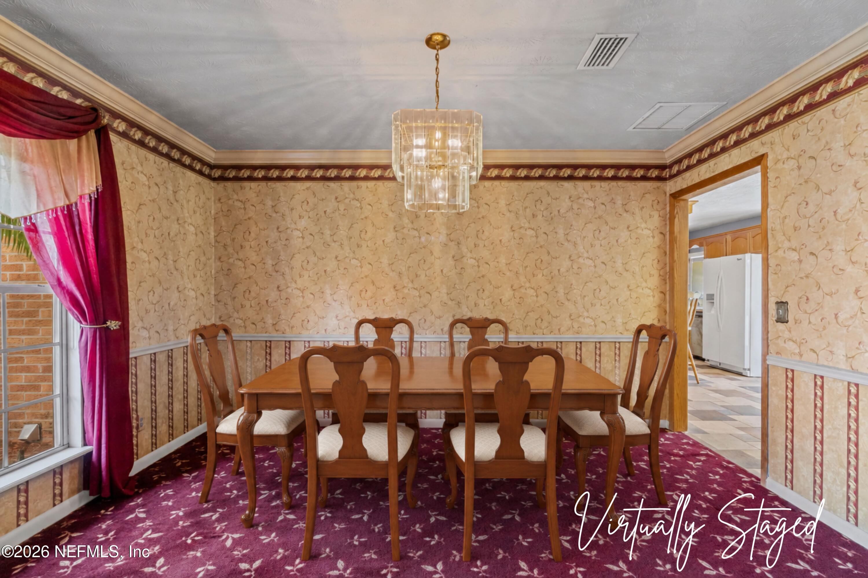 Virtually staged dining room with a wooden table, burgundy carpet, ornate wallpaper, and chandelier.