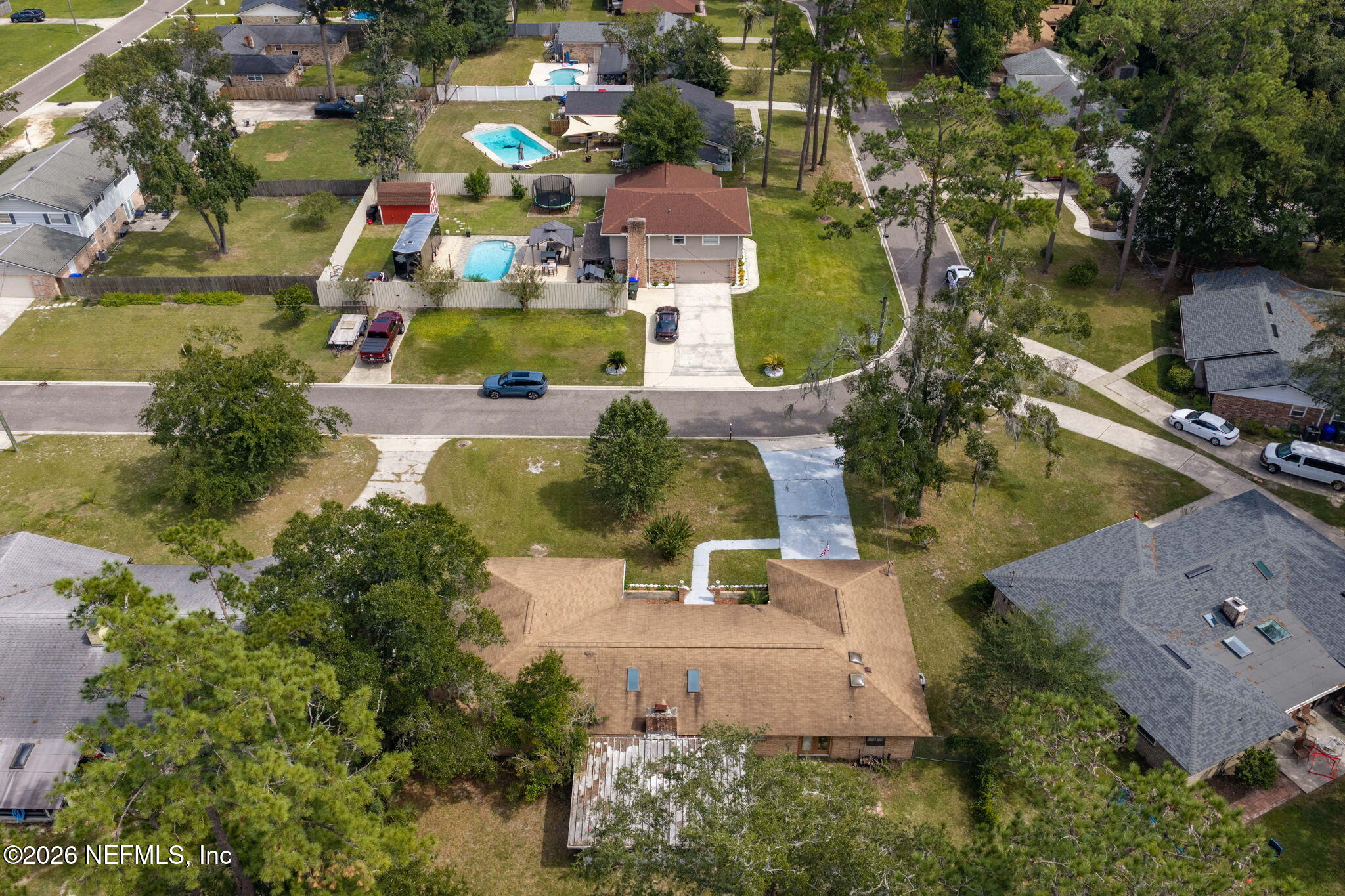 Aerial view of a detached home with a driveway and lawn among neighboring houses.