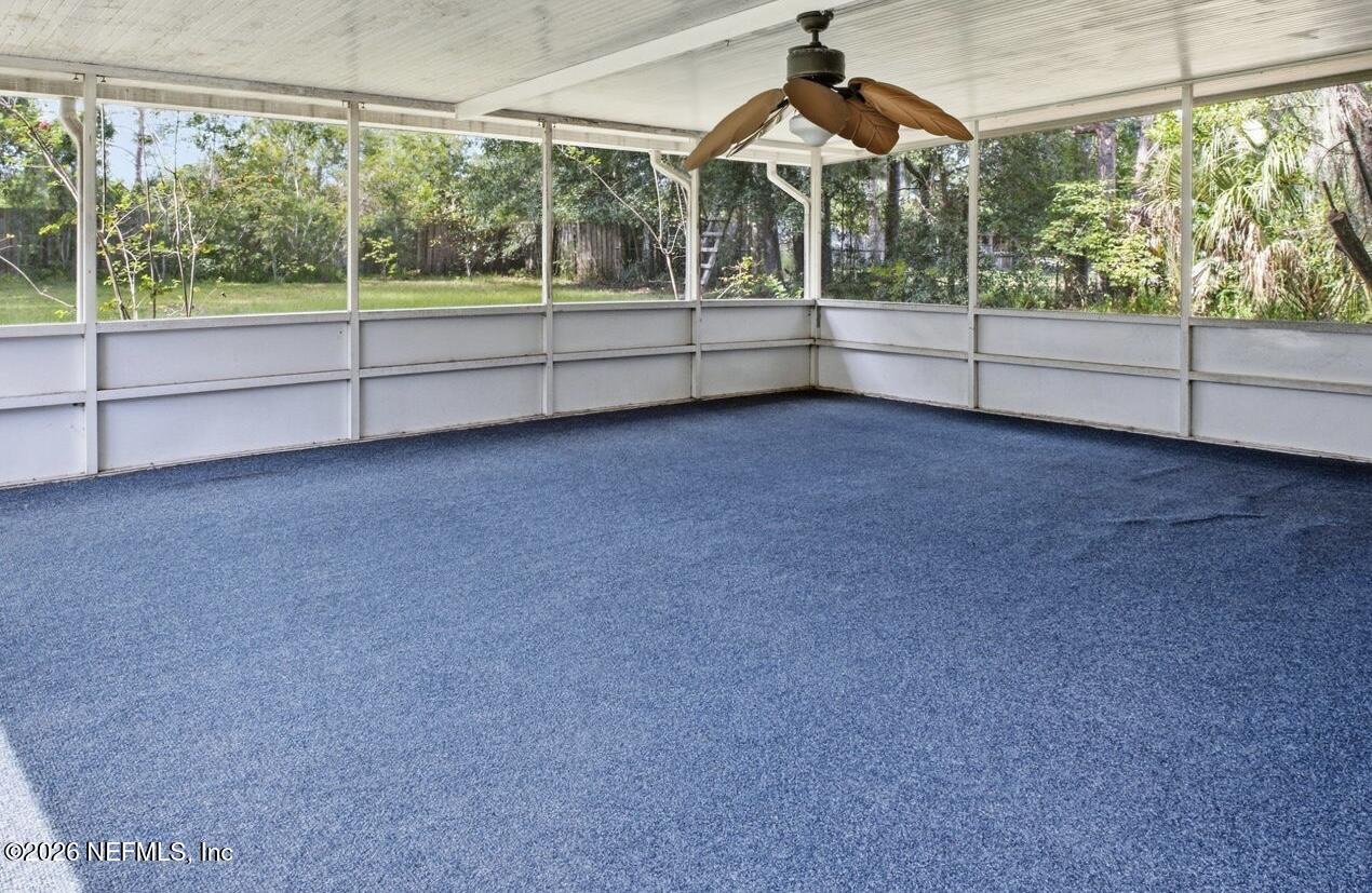Screened porch with blue carpet, a ceiling fan, and a leafy backyard view.
