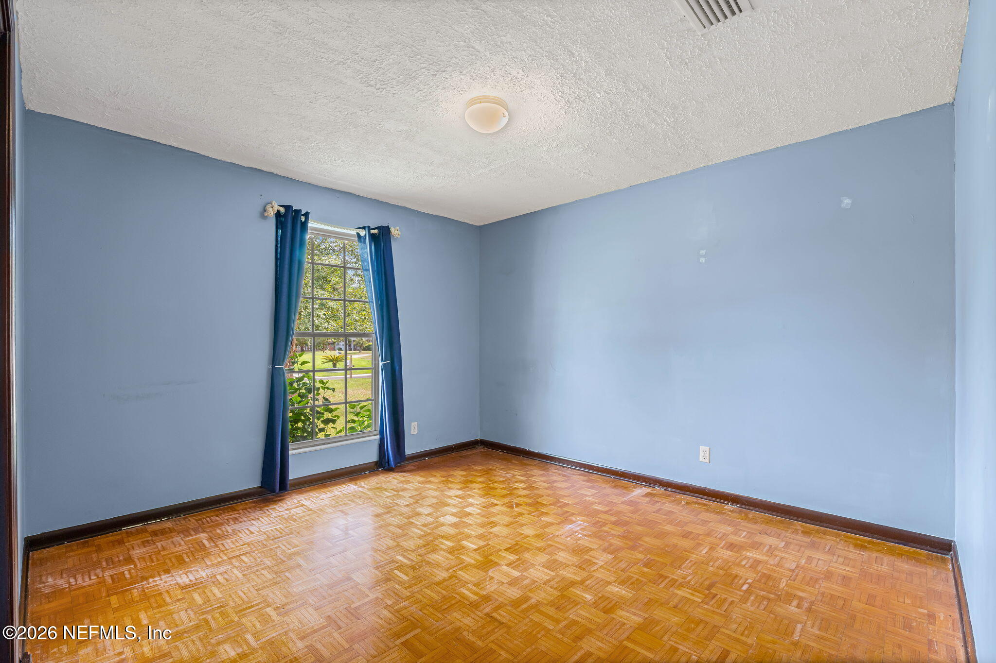 Empty bedroom with blue walls, a curtained window, and parquet flooring.