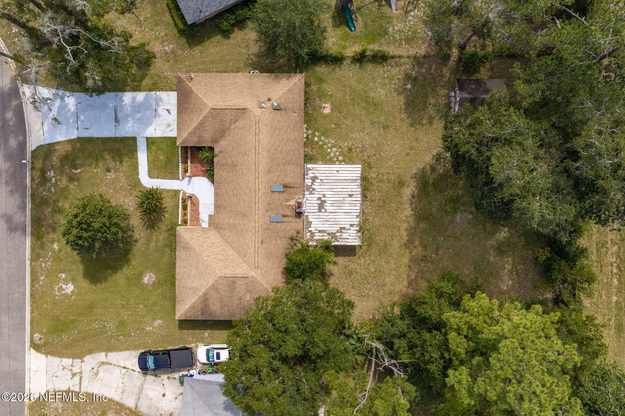 Aerial view of a single-story home, broad lawn, driveway, and weathered rear deck.